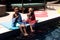 African american brother and sister eating ice creams while sitting at poolside at resort in summer