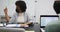 African american businesswoman wearing face mask sitting at desk talking to colleagues in office