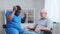African-American caregiver is measuring disabled old man blood pressure. Professional nurse and handicapped patient in a