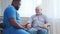 African-American caregiver is measuring disabled old man blood pressure. Professional nurse and handicapped patient in a