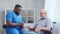 African-American caregiver is measuring disabled old man blood pressure. Professional nurse and handicapped patient in a