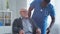 African-American caregiver and old disabled man in a wheelchair. Professional nurse and handicapped patient in a nursing