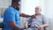 African-American caregiver and old disabled man in a wheelchair. Professional nurse and handicapped patient in a nursing