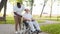 African-American caregiver and old disabled man in a wheelchair. Professional nurse and handicapped patient in the park