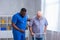African-American caregiver is teaching disabled old man to walk with walker. Professional nurse and handicapped patient