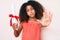 African american child with curly hair holding graduate degree diploma with open hand doing stop sign with serious and confident