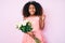 African american child with curly hair wearing princess crown holding flowers screaming proud, celebrating victory and success