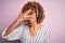 African american curly call center agent woman working using headset over pink background peeking in shock covering face and eyes