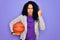 African american curly sportswoman doing sport holding basketball ball over purple background annoyed and frustrated shouting with