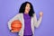 African american curly sportswoman doing sport holding basketball ball over purple background pointing and showing with thumb up