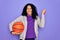 African american curly sportswoman doing sport holding basketball ball over purple background screaming proud and celebrating