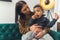 African American cute curled little boy in her mother& x27;s lap eating a cookie sitting on the green sofa studio shot