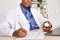 African american doctor writing prescription holding pills bottle sit at desk.