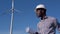African American electrical engineer in a helmet and with a drawing in his hand stands on the background of a windmill