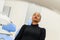 African-American ethnic black patient sitting closing eyes on dental chair waiting for her dentist