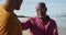 African american father sitting on beach with teenage son, putting hand on his shoulder and talking