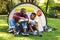 African american father with son having fun and sitting in tent pouring drinks in garden