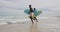 African american father and teenage son running on a beach holding surfboards and talking