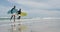 African american father and teenage son running on a beach holding surfboards and talking