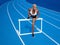 An African American female athlete is running on the Olympic track, executing the hurdle jump over the blue lanes, concept of race