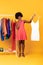 African American Female On Shopping Choosing Outfit, Yellow Background, Vertical