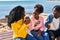 African american friends having breakfast sitting on bench at seaside