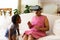 African american girl looking at her grandmother wearing vr headset sitting on the couch at home