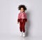 African American girl in a stylish modern red jumpsuit jumps high on a gray background.