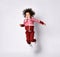 African American girl in a stylish modern red jumpsuit jumps high on a gray background.