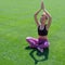 An African American girl in summer in sports clothes raised her hands up and meditates. Young cute black girl sitting on grass in