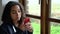 African American girl teenager depressed sitting by a window using her mobile cell phone or smartphone