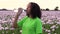 African American girl teenager female young woman walking drinking from a water bottle on path through field of pink poppy flowers