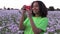 African American girl teenager walking through field of pink poppy flowers taking photographs