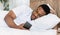 African american guy using cellphone lying in bed in bedroom