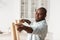 African american handyman working at home, measuring the width between legs of wooden table, assembling furniture