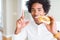 African American hungry man eating hamburger for lunch surprised with an idea or question pointing finger with happy face, number