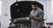 African American male car mechanic looking at an open car engine and talking on a smartphone