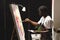 African american male painter wearing face mask painting on canvas in art studio