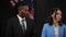 African American male politician giving the floor to Caucasian female spokesperson in camera flashes at press conference