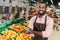 african american male shop assistant in apron standing with crossed arms near fruit department