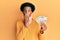 African american man with afro hair wearing cervical neck collar and holding money from insurance covering mouth with hand,