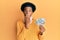 African american man with afro hair wearing cervical neck collar and holding money from insurance covering mouth with hand,