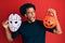 African american man with afro hair wearing hockey mask and halloween pumpking angry and mad screaming frustrated and furious,