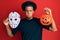 African american man with afro hair wearing hockey mask and halloween pumpking puffing cheeks with funny face
