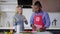 African American man in apron cutting cucumber for veggie salad as Caucasian woman entering kitchen in slow motion