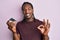 African american man with braids holding chocolate cake doing ok sign with fingers, smiling friendly gesturing excellent symbol