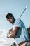 African american man in cap and sunglasses holding club and playing golf