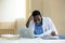 African American man doctor unhappy boring hand touching head using laptop and holding paperwork checking report.