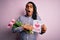African american man with dreadlocks holding love mom message and tulips on mothers day scared in shock with a surprise face,