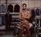 African-American man dressed in a trendy elegant suit posing with crossed arms near retro sports motorbike at the men`s